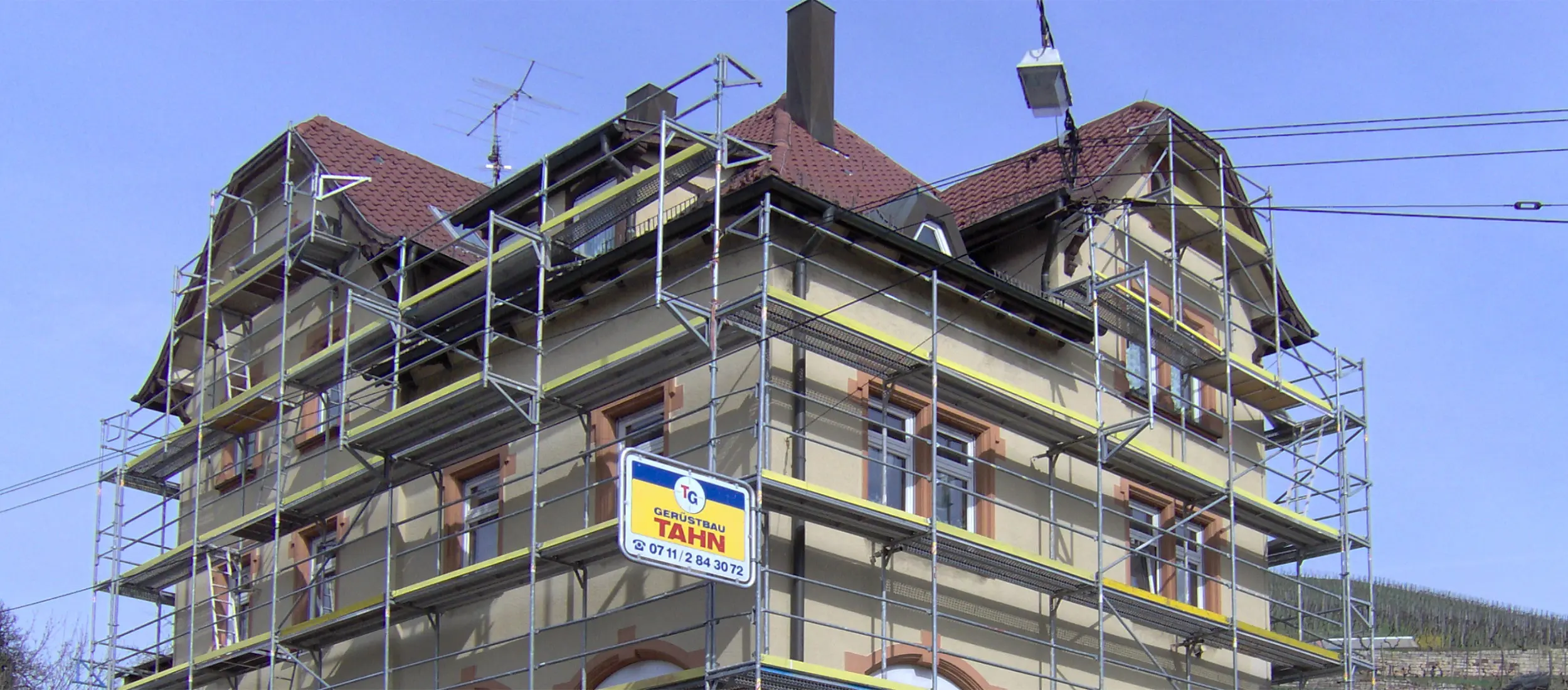 Eingerüstetes Altbau-Wohnhaus mit Tahn-Werbebanner am Gerüst